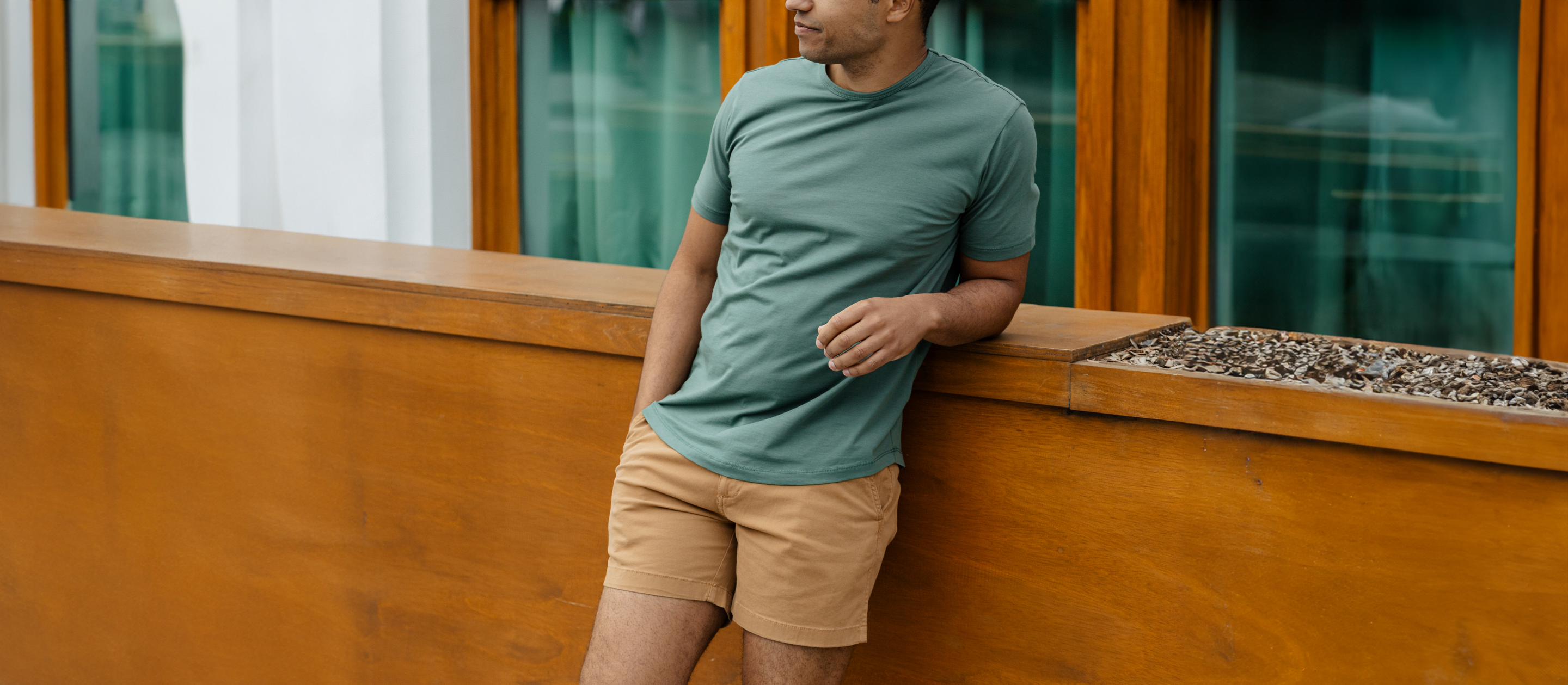 Man leaning against balcony wearing Supima Tee Dark Sage and Stretch Short Camel